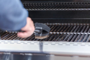 A man cleans grill grates before storing a gas grill for winter